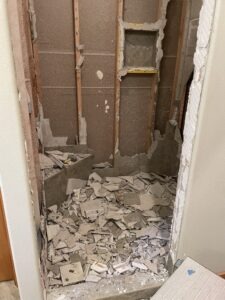 Remnants of a tile shower. Framing is visible. The entire floor is full of smashed shower tiles. 