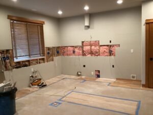 Another kitchen wall after cabinets have been removed. Some pieces of drywall have been removed and the pink insulation is exposed. 